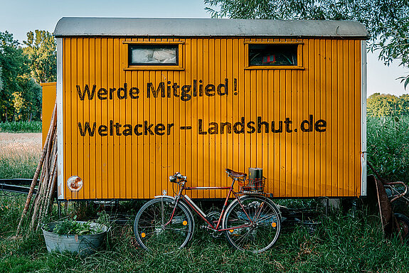 oranger Bauwagen mit der Aufschrift: Werde Mitglied! Weltacker-Landshut.de