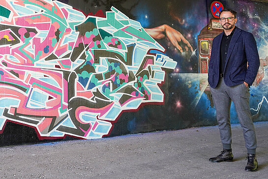 Der Künstler und sein Kunstwerk: Kai Hockenberger vor dem neuen Graffiti an der Unterführung an der Schleifermoosach. (Foto: Stadt Freising)