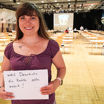 Finanzreferentin Monika Schwind hält ein Schild mit der Aufschrift: "weil Demokratie die Rechte aller wahrt."