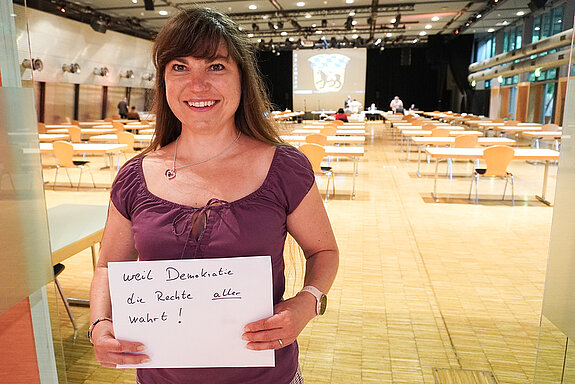 Finanzreferentin Monika Schwind hält ein Schild mit der Aufschrift: "weil Demokratie die Rechte aller wahrt."