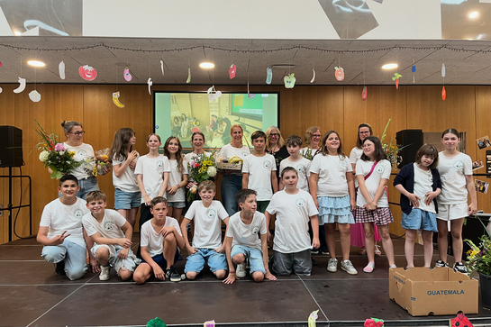 Im Vordergrund viele Kinder in wei&szlig;en T-Shirts, dahinter Lehrerinnen, teilweise mit Blumen. Alle lachen.