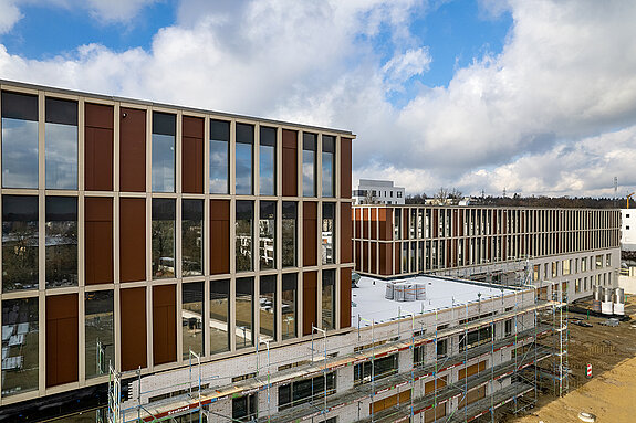 Dank der guten Fortschritte beim Neubau der SteinPark-Schulen kann jetzt auch die glänzende Klinkerfassade mit den Glas-Beton-Elementen bewundert werden. (Drohnenfoto: F.J. Kirmaier/das produktionshaus)