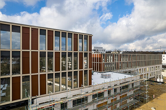 Dank der guten Fortschritte beim Neubau der SteinPark-Schulen kann jetzt auch die glänzende Klinkerfassade mit den Glas-Beton-Elementen bewundert werden. (Drohnenfoto: F.J. Kirmaier/das produktionshaus)