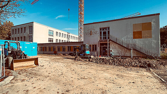 Das Foto zeigt von außen die beiden Bestandsgebäude der Schule und davor die Baustelle.