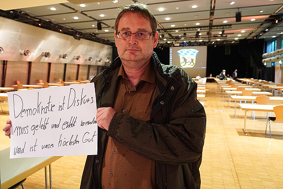 Stadtrat Richard Paukner hält ein Schild mit der Aufschrift: "Demokratie ist Diskurs, muss gelebt und erlebt werden und ist unser höchstes Gut."