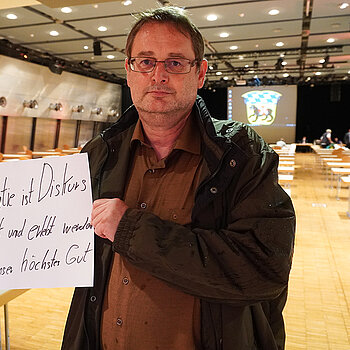 Stadtrat Richard Paukner hält ein Schild mit der Aufschrift: "Demokratie ist Diskurs, muss gelebt und erlebt werden und ist unser höchstes Gut."