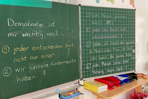 Tafel mit Schrift: Demokratie ist mir wichtig, weil... 1 jeder entscheiden darf, nicht nur einer. 2 wir unsere Kinderrechte haben, 3 jeder Mensch gleich viel zählt...