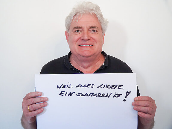 Stadtratsmitglied Sebastian Habermeyer. Foto: Stadt Freising Ein Mann in einem schwarzen Hemd zeigt ein Schild mit der Aufschrift "weil alles andere ein Schmarrn ist!"