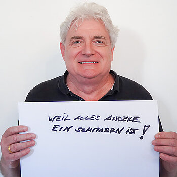 Stadtratsmitglied Sebastian Habermeyer. Foto: Stadt Freising Ein Mann in einem schwarzen Hemd zeigt ein Schild mit der Aufschrift "weil alles andere ein Schmarrn ist!"