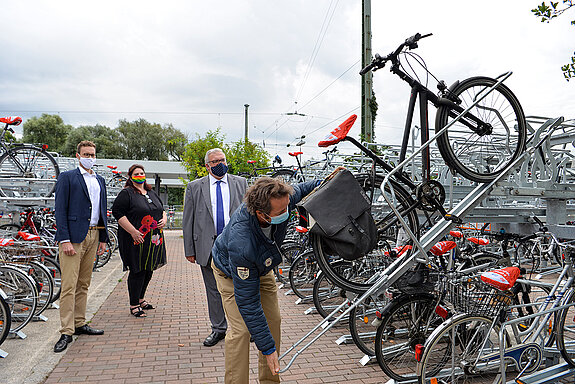 Marco Ladenthin und Mareike Schoppe (DB) sowie MdB Erich Irlstorfer (v.l.) schauen interessiert zu, wie das Rad auf den Bügel gesetzt wird. (Foto: Stadt Freising)
