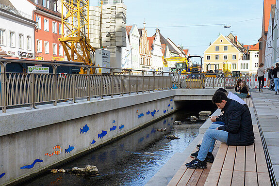 Sich gemütlich auf den Sitzstufen niederlassen, das wird bereits während der Bauarbeiten praktiziert. Im Bild ist auch das Fischmosaik zu sehen. (Foto: Stadt Freising) 