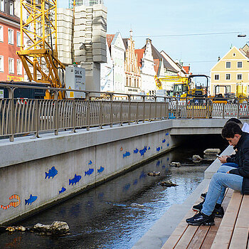 Sich gemütlich auf den Sitzstufen niederlassen, das wird bereits während der Bauarbeiten praktiziert. Im Bild ist auch das Fischmosaik zu sehen. (Foto: Stadt Freising) 