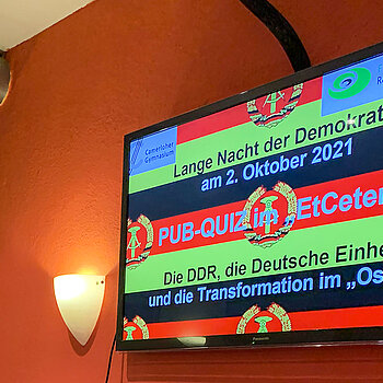 Bildschirm mit DDR-Emblem auf Schwarz-Rot-Gold und "Pub-Quiz im EtCetera"