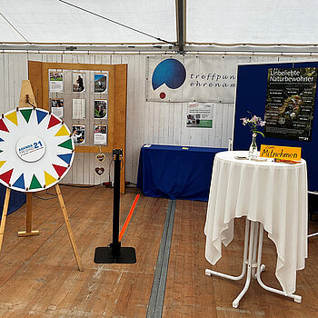 Ein Stand mit buntem Glücksrad, Stehtisch und kleinem Bildschirm 