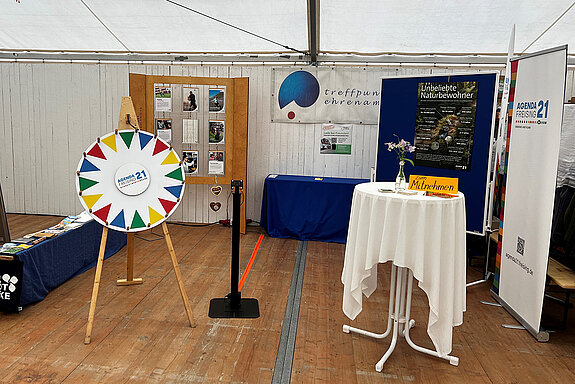 Ein Stand mit buntem Glücksrad, Stehtisch und kleinem Bildschirm 