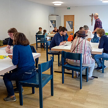 An mehreren Tischen sitzen Menschen beim Spielen zusammen. 
