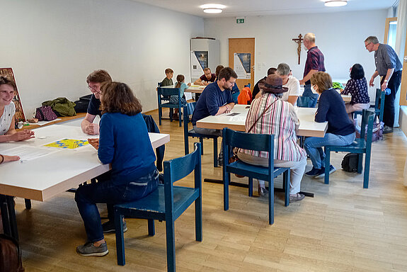 An mehreren Tischen sitzen Menschen beim Spielen zusammen. 
