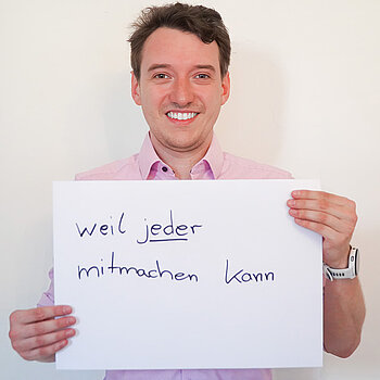Stadtratsmitglied Daniel Hubensteiner. Foto: Stadt Freising Ein Mann in einem rosa Hemd zeigt ein Schild mit der Aufschrift "weil jeder mitmachen kann"