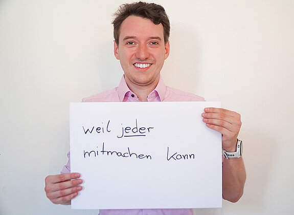 Stadtratsmitglied Daniel Hubensteiner. Foto: Stadt Freising Ein Mann in einem rosa Hemd zeigt ein Schild mit der Aufschrift "weil jeder mitmachen kann"
