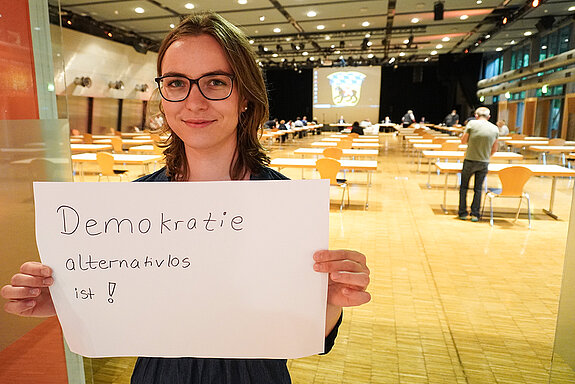 Stadträtin Emilia Kirner hält ein Schild mit der Aufschrift: "weil Demokratie alternativlos ist!"