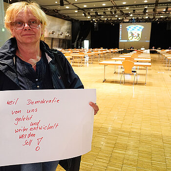 Stadträtin Johanna Hiergeist hält ein Schild mit der Aufschrift: "weil Demokratie von uns gelebt und weiterentwickelt werden soll!"