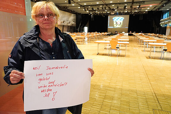 Stadträtin Johanna Hiergeist hält ein Schild mit der Aufschrift: "weil Demokratie von uns gelebt und weiterentwickelt werden soll!"