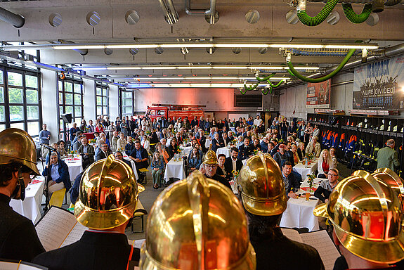 Blick über die Helme des Feuerwehrchors auf die voll besetze Halle der Feuerwache. (Foto: Stadt Freising)