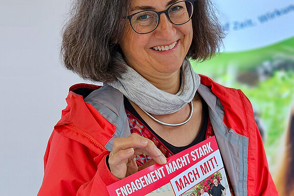 Eine Frau mit dem Plakat der Aktionswoche in rot, blau, weiß "Engagement macht stark"