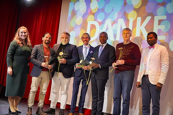 Auf dem Bild ist die Jury vom Interkulturellen Preis 2025 zu sehen: Michaela John, Mauricio Tercero, Sebastian Wanzke, Jürgen Mieskes, Samuel Fosso, Jochen Hauer und Sem Haikali.