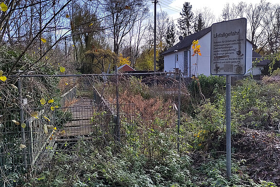 eine Fußgängerbrücke mit fehlenden Planken abgesperrt und zugewuchert.