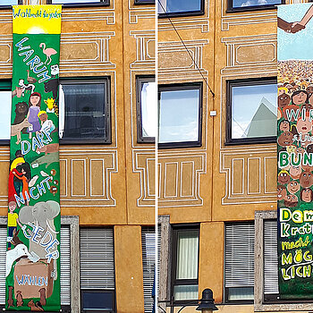 Bunte Banner, 7 Meter lang an einer Fassade: viele Gesichter, darüber ein Handschlag, mit dem Text: Wir sind Bunt, Demokratie macht es möglich ?!