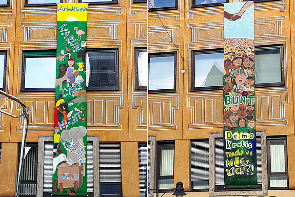 Bunte Banner, 7 Meter lang an einer Fassade: viele Gesichter, darüber ein Handschlag, mit dem Text: Wir sind Bunt, Demokratie macht es möglich ?!