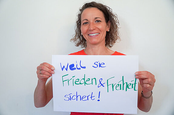 Stadtratsmitglied Dr. Carolin Adldinger. Foto: Stadt Freising Eine Frau in einem orangenen T-Shirt zeigt ein Schild mit der Aufschrift "weil sie Frieden & Freiheit sichert"