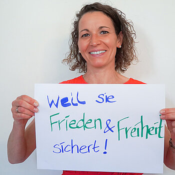 Stadtratsmitglied Dr. Carolin Adldinger. Foto: Stadt Freising Eine Frau in einem orangenen T-Shirt zeigt ein Schild mit der Aufschrift "weil sie Frieden & Freiheit sichert"