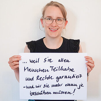 Stadtratsmitglied Teresa Degelmann. Foto: Stadt Freising Eine Frau mit Brille und einem schwarzen T-Shirt zeigt ein Schild mit der Aufschrift "weil sie allen Menschen Teilhabe und Rechte gewährt- und wir sie mehr denn je beschützen müssen!"