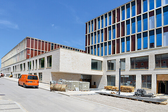 Etwas verdeckt von aufgestapeltem Baumaterial: der Haupteingang, der über das Forum zur Grundschule (ganz links im Bild) und zur Mittelschule (rechts) führt. (Foto: Stadt Freising)