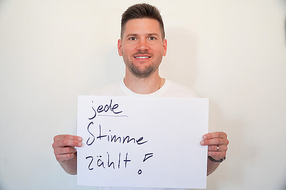 Stadtratsmitglied Daniel Pellmeyer. Foto: Stadt Freising Ein Mann in einem weißen T-Shirt zeigt ein Schild mit der Aufschrift "jede Stimme zählt"
