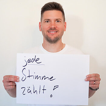 Stadtratsmitglied Daniel Pellmeyer. Foto: Stadt Freising Ein Mann in einem weißen T-Shirt zeigt ein Schild mit der Aufschrift "jede Stimme zählt"