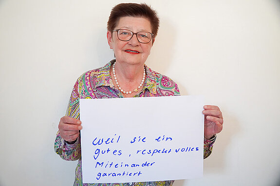 Stadtratsmitglied Eva Boenig. Foto: Stadt Freising Eine Frau in einem rosa, gelb und grünen Hemd zeigt ein Schild mit der Aufschrift "weil sie ein gutes, respektvolles Miteinander garantiert"