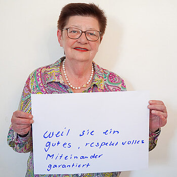 Stadtratsmitglied Eva Boenig. Foto: Stadt Freising Eine Frau in einem rosa, gelb und grünen Hemd zeigt ein Schild mit der Aufschrift "weil sie ein gutes, respektvolles Miteinander garantiert"