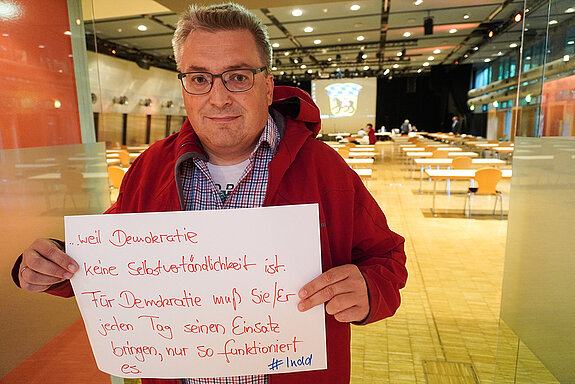 Werner Habermeyer hält ein Schild mit der Aufschrift: "...weil Demokratie keine Selbstverständlichkeit ist. Für Demokratei muss sie/er jeden Tag seinen Einsatz bringen, nur so funktioniert es."