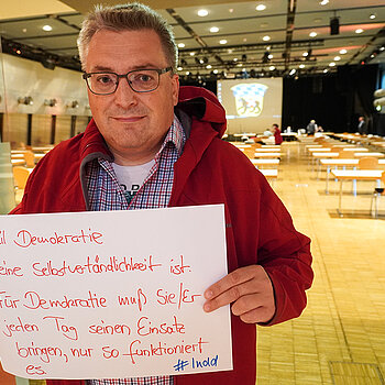 Werner Habermeyer hält ein Schild mit der Aufschrift: "...weil Demokratie keine Selbstverständlichkeit ist. Für Demokratei muss sie/er jeden Tag seinen Einsatz bringen, nur so funktioniert es."