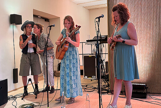 Das Foto zeigt vier Musikerinnen bei Singen und Spielen.