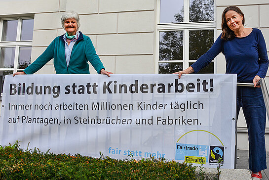 Ursula Blum und Monika Hobmair vom Fairen Forum zeigen ein Transparent mit der Aufschrift "Bildung statt Kinderarbeit!" im Rahmen der Aktion zur Fairen Woche 2020