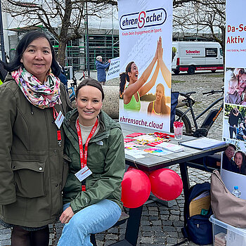 Die Caritas stellte ihre Projekte vor. Foto: Caritas zwei Frauen vor Rollups mit Luftballons, im Hintergrund eine Person in Warnjacke