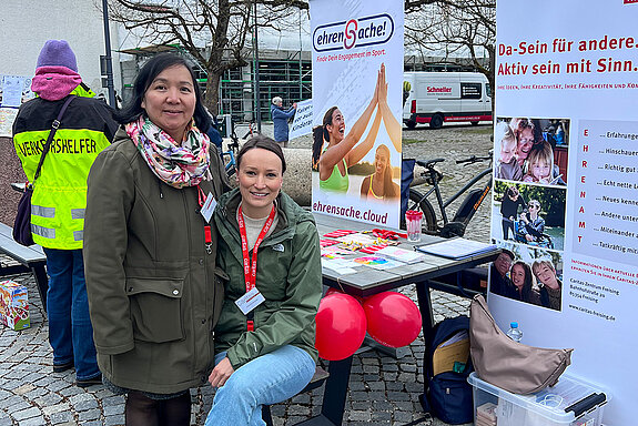 Die Caritas stellte ihre Projekte vor. Foto: Caritas zwei Frauen vor Rollups mit Luftballons, im Hintergrund eine Person in Warnjacke