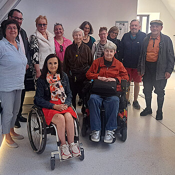 Gruppenbild mit 2 Rollstuhlfahrerinnen in einem Raum mit Dachschräge
