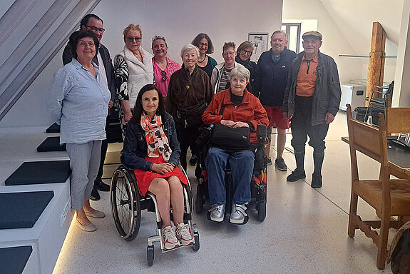 Gruppenbild mit 2 Rollstuhlfahrerinnen in einem Raum mit Dachschräge