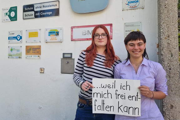 Vivienne Greiner und Afra Danzl feiern die Demokratie, weil sie sich frei entfalten können. Foto: Herzer Zwei junge Frauen stehen vor dem Josef Hofmiller Gymnasium mit Schildern an der Wand. Unter anderem "Schule ohne Rassismus"
