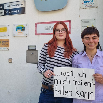 Vivienne Greiner und Afra Danzl feiern die Demokratie, weil sie sich frei entfalten können. Foto: Herzer Zwei junge Frauen stehen vor dem Josef Hofmiller Gymnasium mit Schildern an der Wand. Unter anderem "Schule ohne Rassismus"